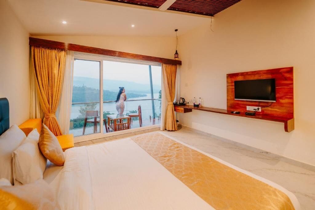 Ein Hotelzimmer mit einem großen Bett, einem an der Wand montierten Fernseher, einem Balkon mit Aussicht und einem Tisch mit Stühlen.