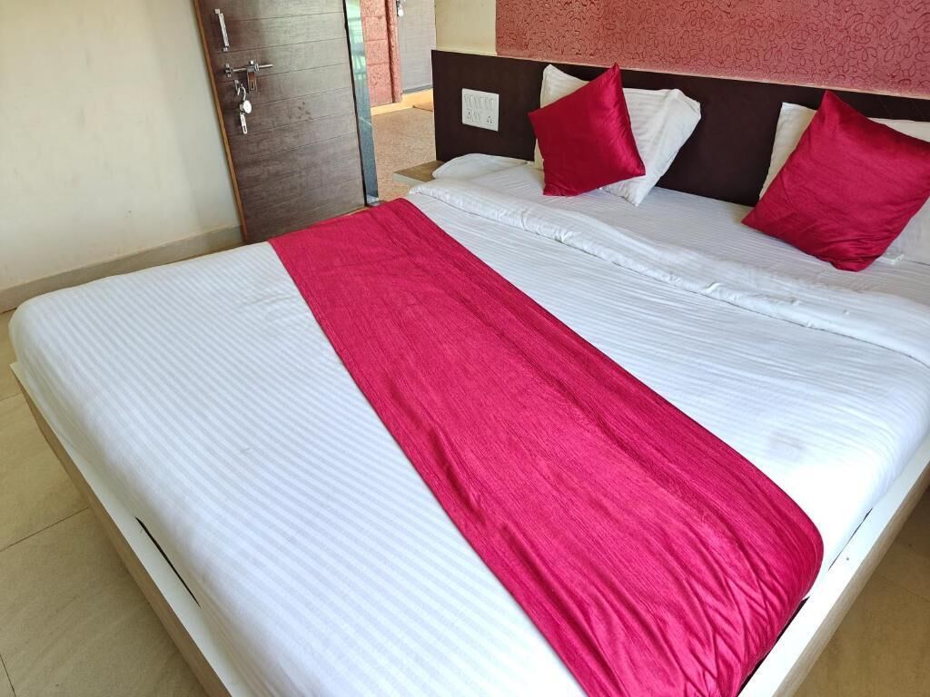 Ein Bett mit weißer Bettwäsche und einer roten Tagesdecke, ein hölzernes Kopfende und eine Tür mit Schlüsselsperre.