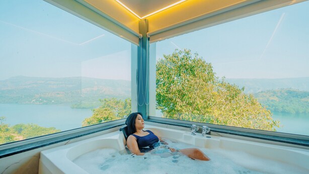 A person relaxing in a bathtub with a view of a lake and hills. - Nisarga Lake Resort Tapola (Mahabaleshwar)