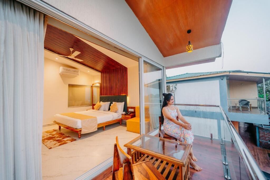 A modern hotel room with a balcony, a bed, a sitting area, and a view of the outside.