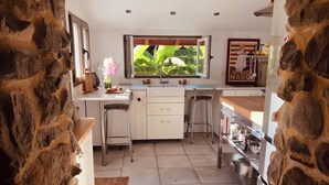 A kitchen with white cabinets, a stone wall, a window with a view of greenery, and a hanging pot rack. - Nature gite (2 suites) near Espellette and Cambo les bains Pets welcome (Itxassou)