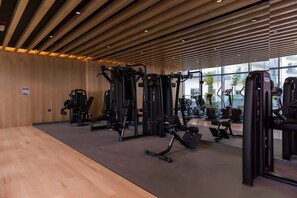 Een sportschool met diverse fitnessapparaten, houten vloeren en grote ramen.