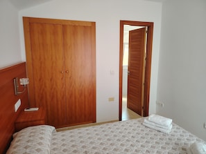 Una camera da letto con un'armadio in legno, un letto con copripiumino decorato e una porta del bagno a vista.
