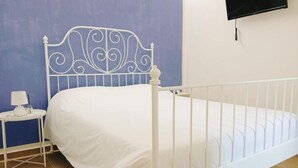 Una cama de metal blanco con cabecera decorativa, una mesita de noche con lámpara y un televisor montado en la pared.