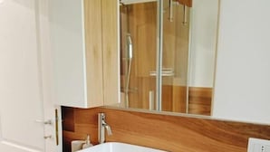 Un baño moderno con un lavamanos blanco, tocador de madera y un espejo grande.