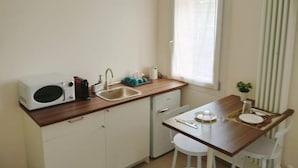 Cocina compacta con microondas, lavamanos y un pequeño comedor con taburetes.