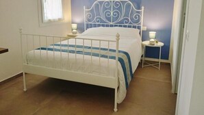 Una cama con estructura metálica blanca, colcha azul y blanca, y dos mesitas de noche con lámparas.