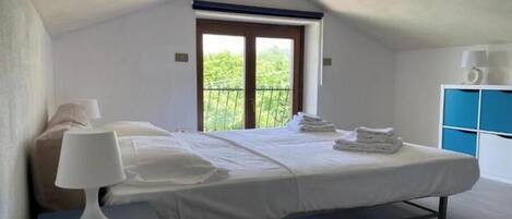 Un dormitorio con cama, lámpara de noche, ventana y vistas al verdor.