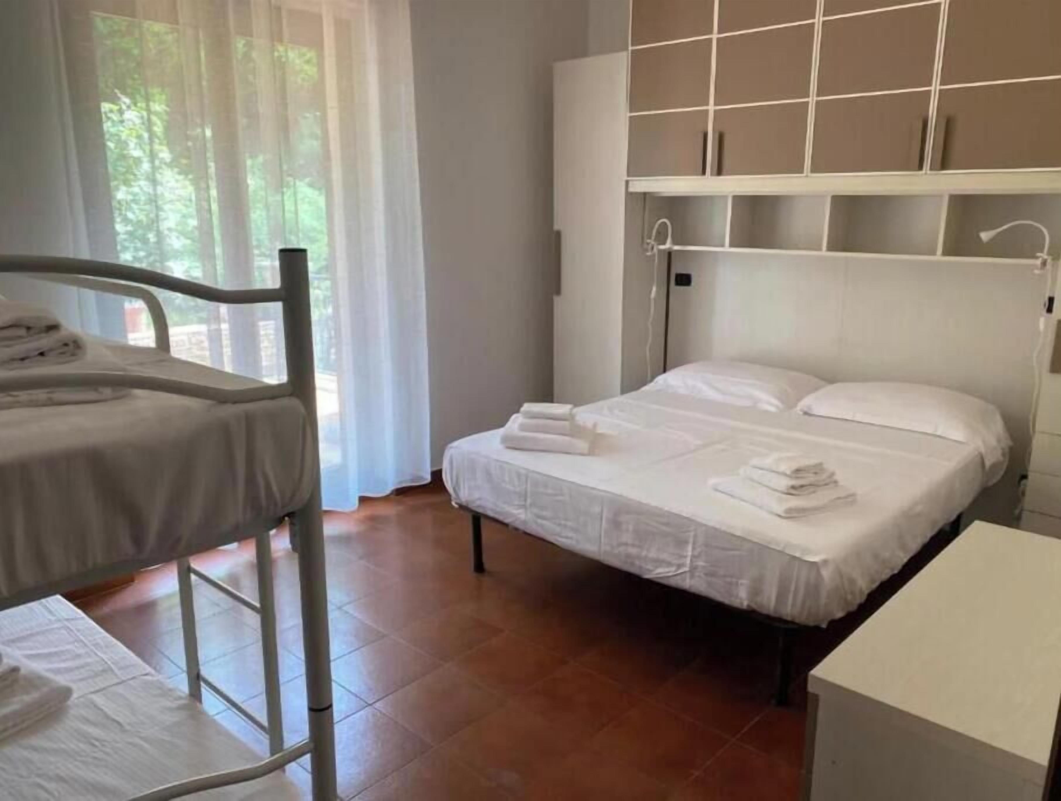 A room with a bunk bed, a single bed, a wardrobe, and a window with curtains.