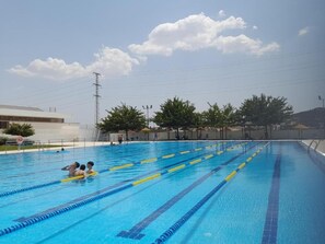 A swimming pool with clear lanes, a lifeguard stand, and a building in the background.