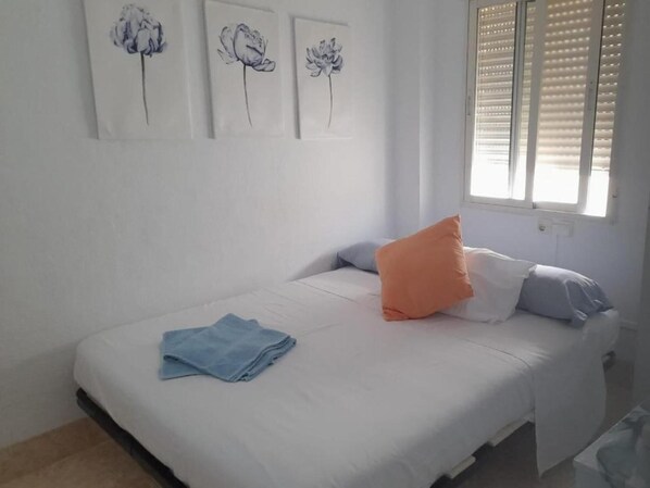 A bedroom with a bed, pillows, a window with blinds, and wall art.