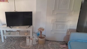 Un salon avec un téléviseur posé sur un meuble, un fauteuil bleu, une porte blanche et un sol à motifs.