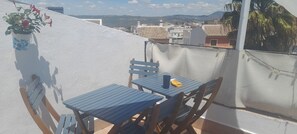 A balcony with a table and chairs, a potted plant, and a view of the cityscape.