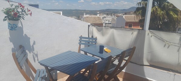 Un balcon avec une table et des chaises, un pot de fleurs et une vue sur le paysage urbain.