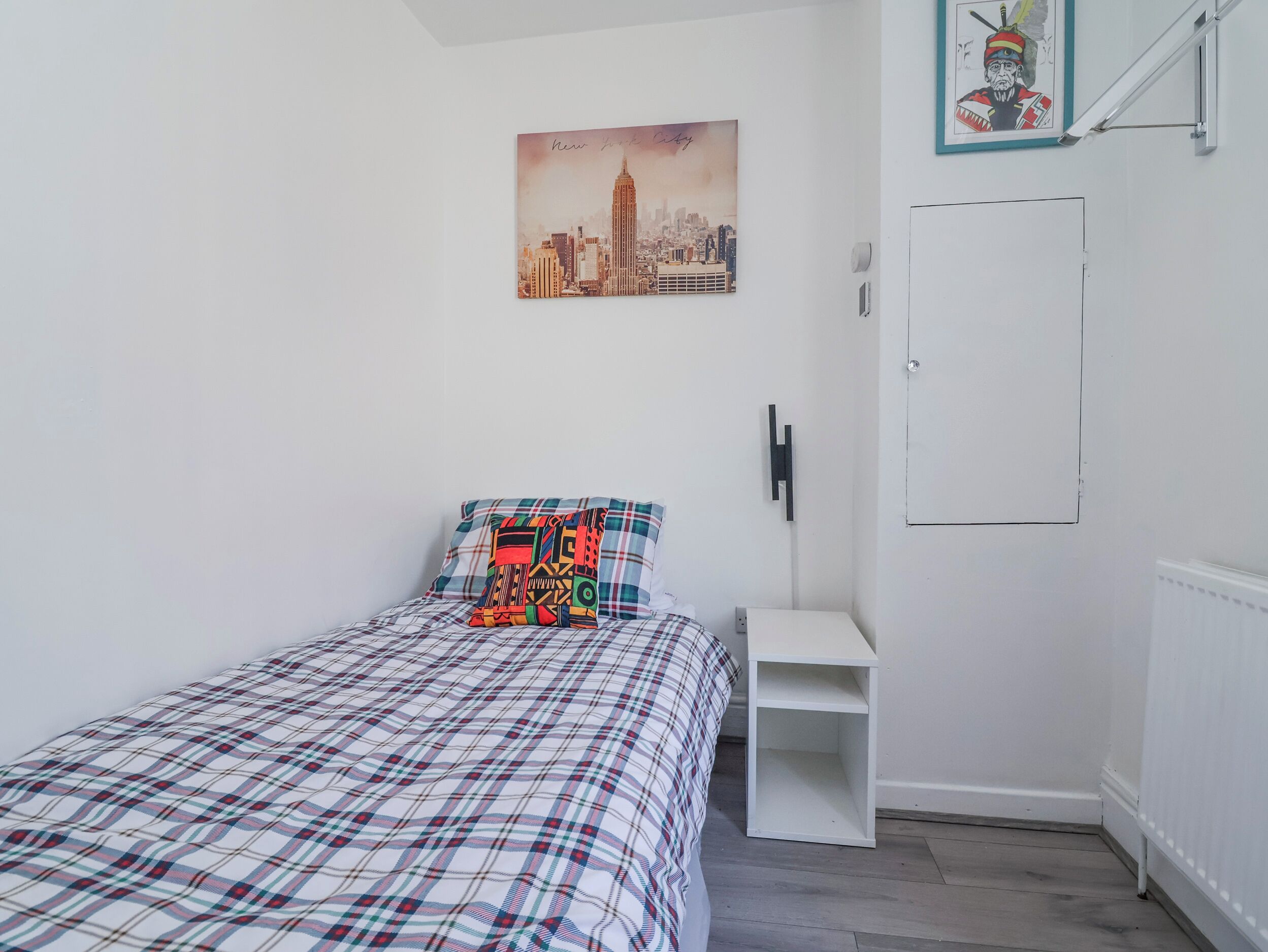 Ein Schlafzimmer mit Bett, Kissen, Nachttisch, einer Tür und einem an der Wand hängenden Bild.