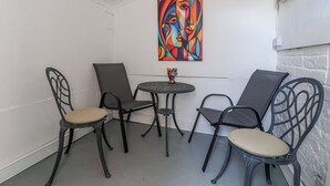 Un petit patio clos, avec une table ronde et quatre chaises, une peinture abstraite aux couleurs vives accrochée au mur et un mur en briques blanches.