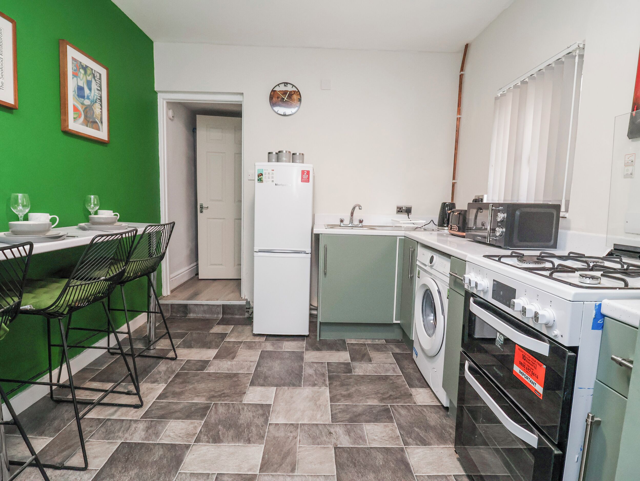 Cocina compacta con lavadora, estufa, microondas y comedor con sillas.