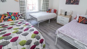 Une chambre avec deux lits, une commode, une fenêtre avec des rideaux et un tableau au mur.