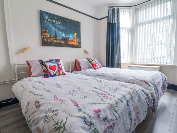 A hotel room with two beds, floral bedding, a cityscape artwork, and a window with curtains. - Ince Lodge (Liverpool)