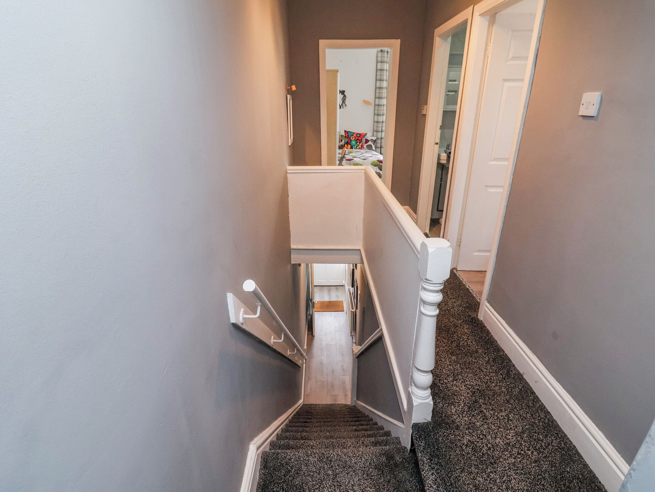 Una escalera con barandilla, peldaños alfombrados y una puerta blanca al final.