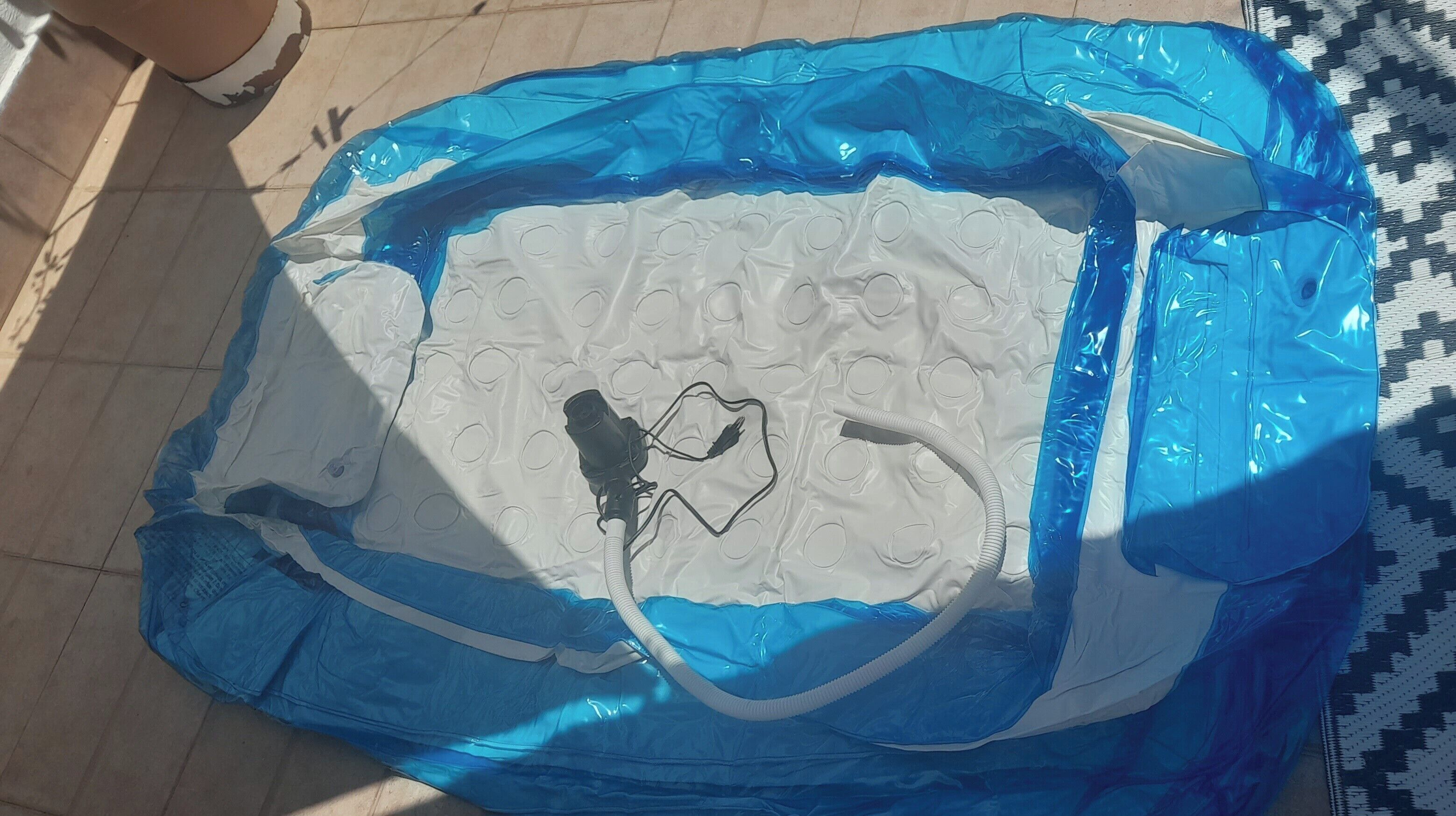 An inflatable pool with a blue and white color scheme, a pump, and a hose.