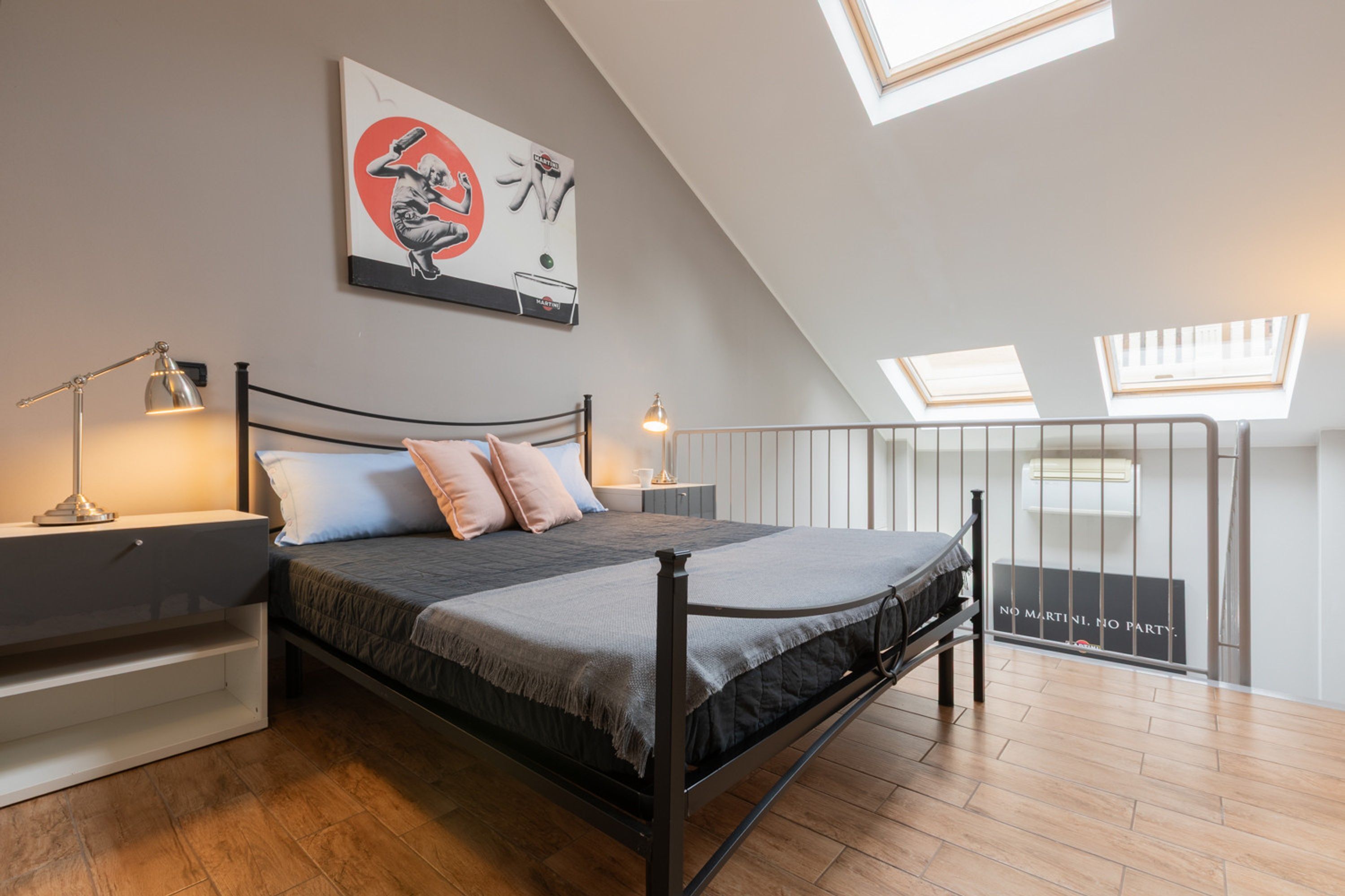 A bedroom with a bed, bedside tables, a nightstand, a skylight, and a view of the outside.