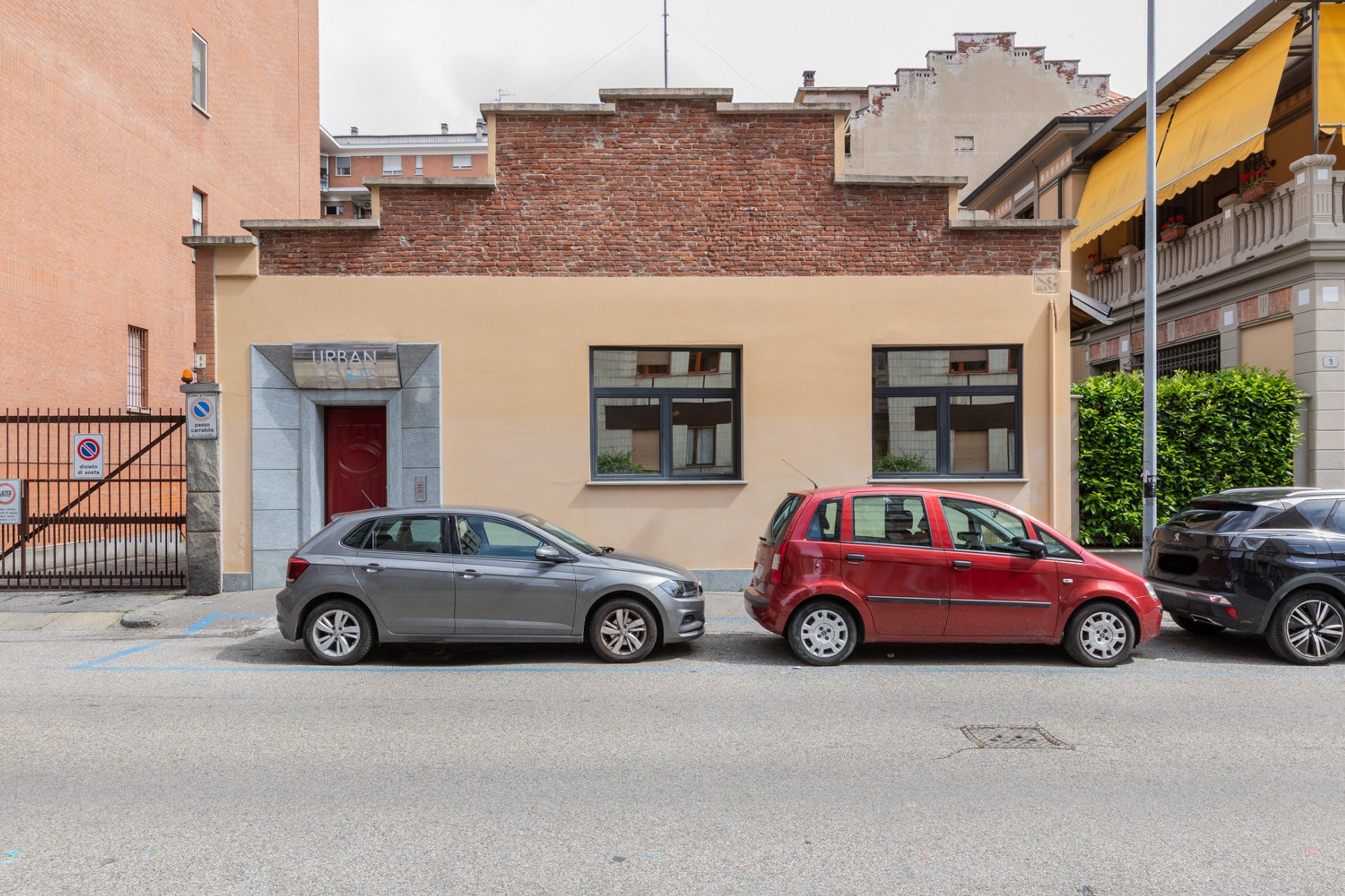 Un immeuble à la façade en briques, avec une porte rouge et deux voitures garées devant.