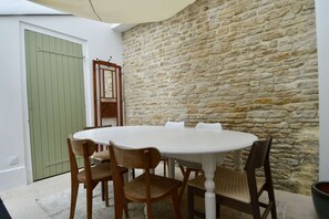 A stone wall, a round table, and wooden chairs in a room. - Maison Yumi - With terrace, near the beach (Saint-Aubin-sur-Mer)