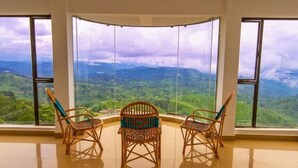 A room with large windows offering a view of green hills and a cloudy sky.