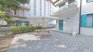 A courtyard with a picnic table and umbrella, surrounded by buildings with balconies and a blue door. - Great accommodation for a relaxing stay (Lignano Sabbiadoro)