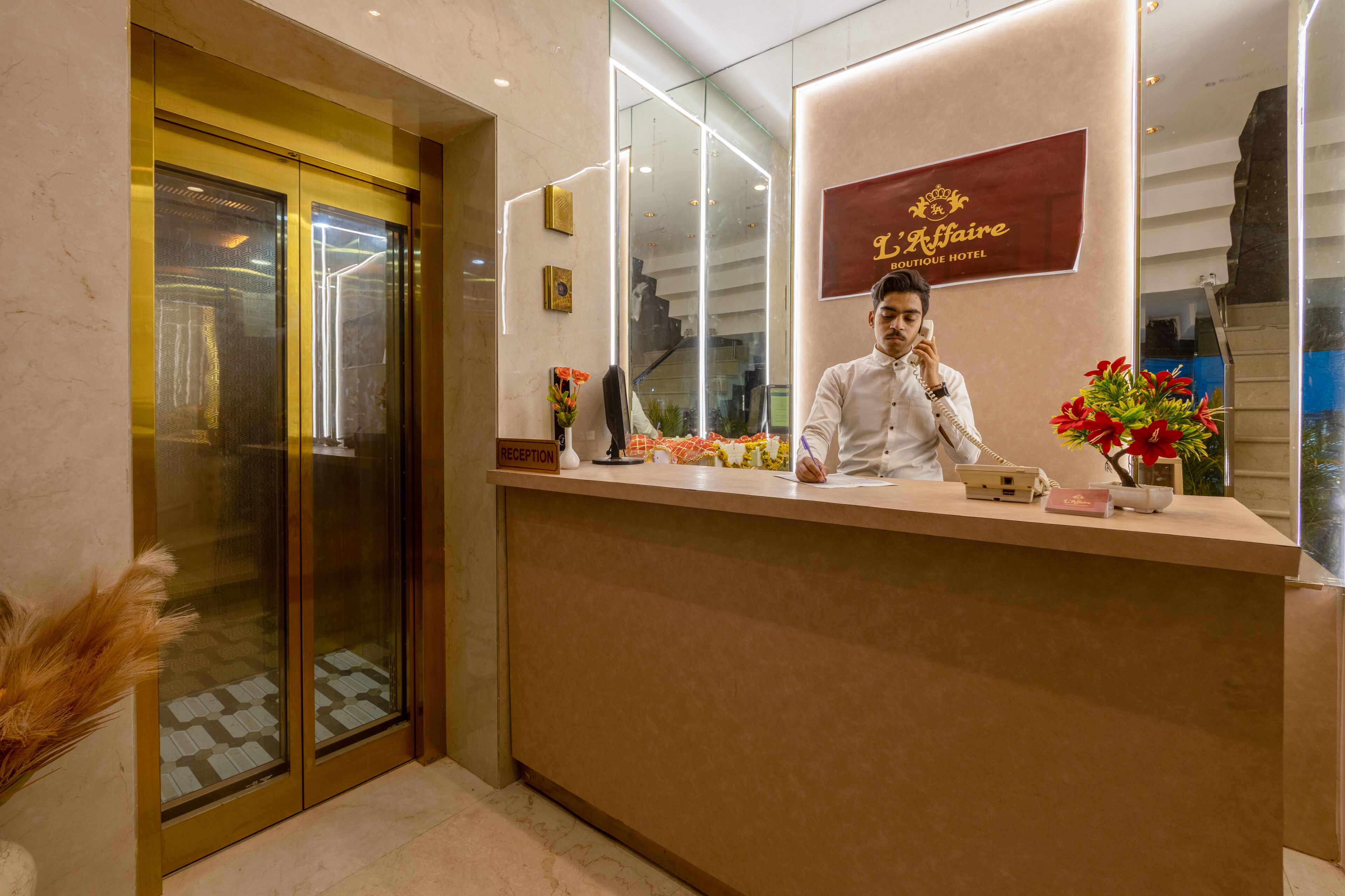 A hotel reception desk with a sign reading 'L'Affaire Boutique Hotel,' a reception counter, a telephone, and a vase with flowers.