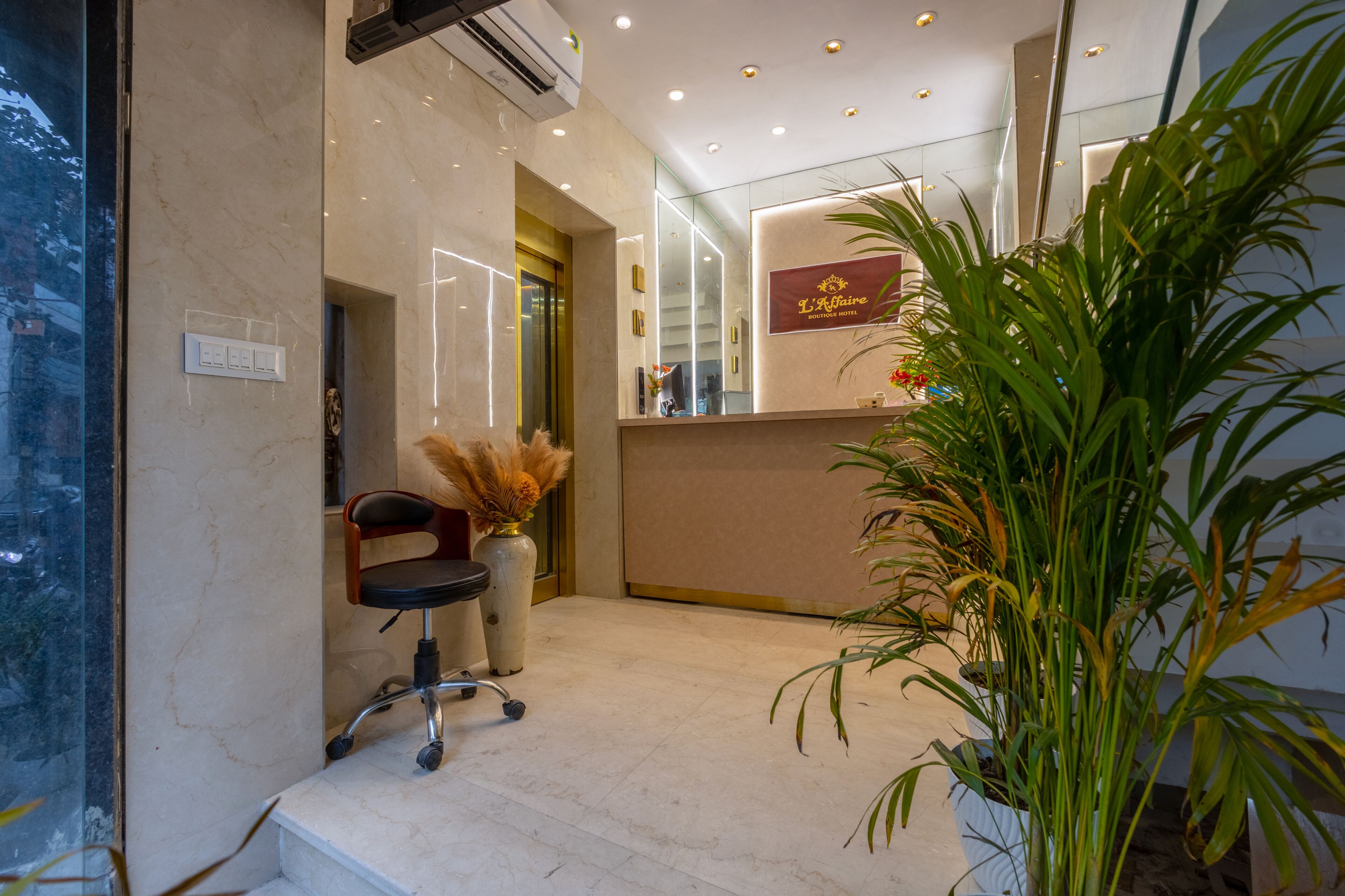 A hotel reception area with a marble floor, a reception desk, a chair, and a large potted plant.