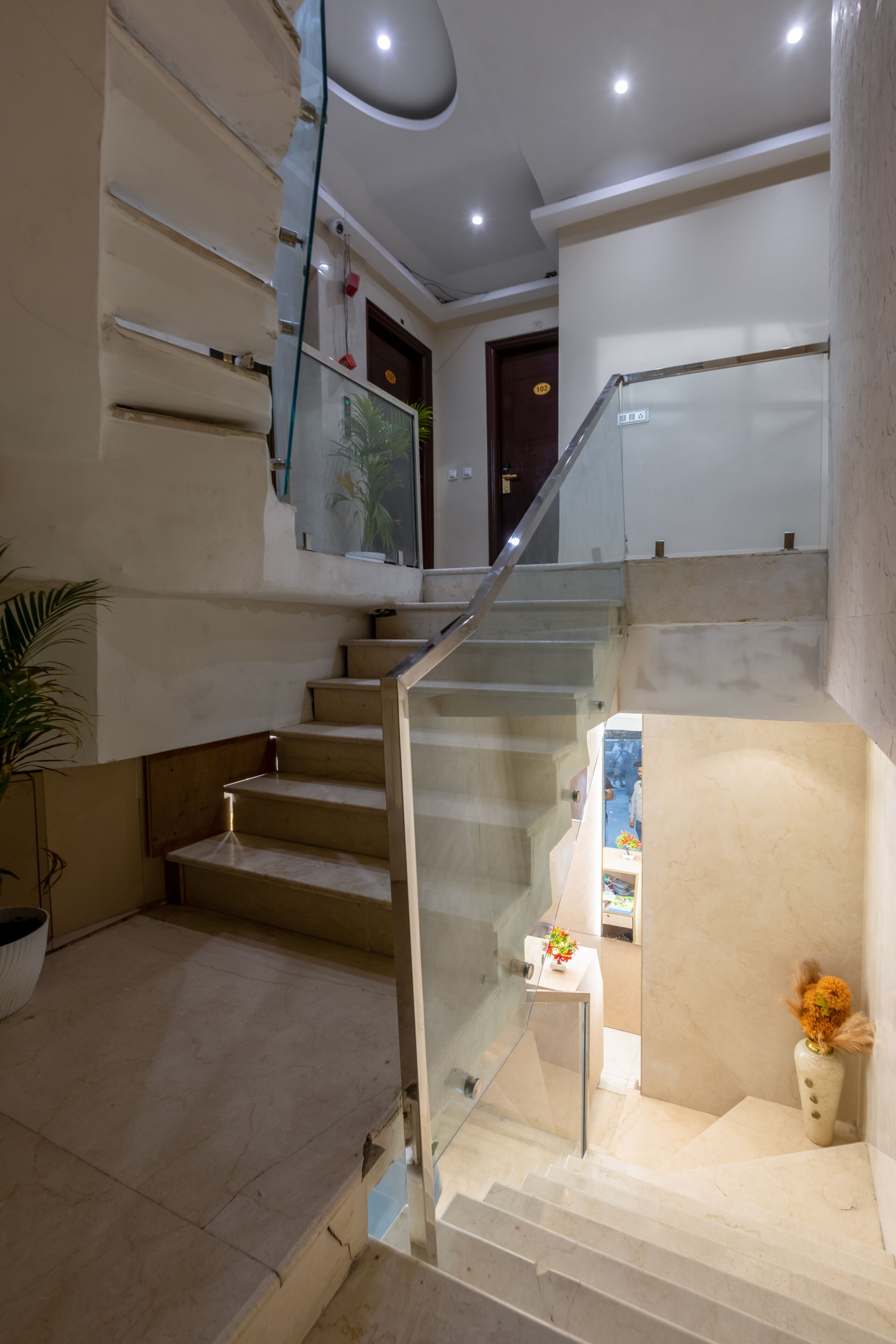 A multi-level interior with a glass railing staircase, a potted plant, and a small table with a vase.