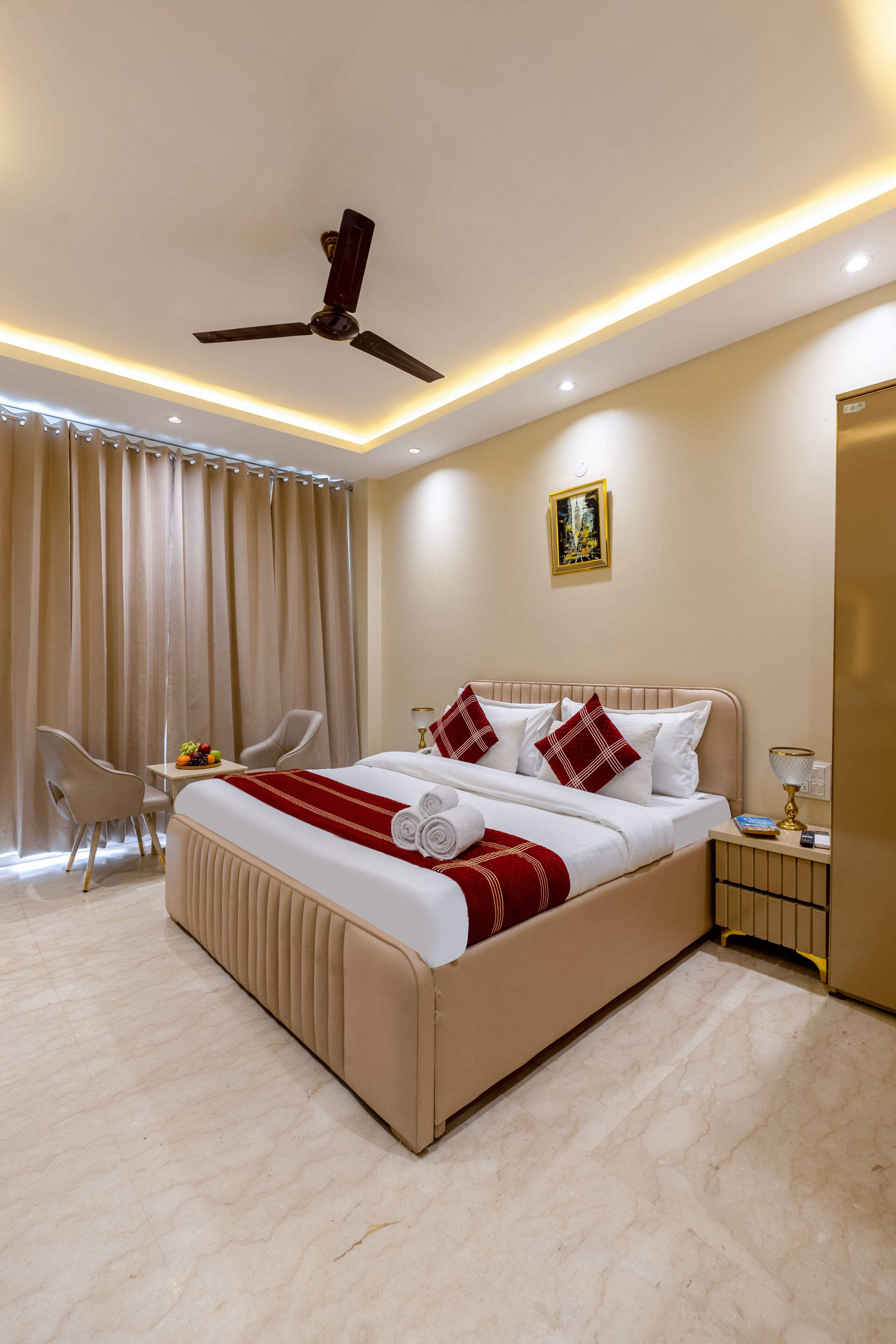 Habitación de hotel con cama, ventilador de techo, mesita de noche, lámpara, silla y cortina.