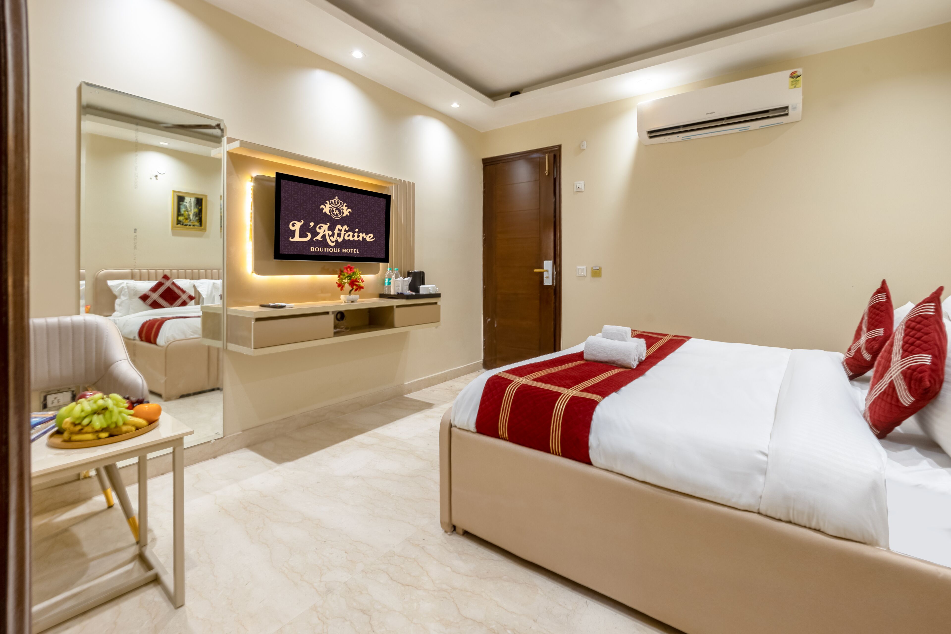 A hotel room with a bed, a desk, a chair, a mirror, and a TV displaying 'L'Affaire Boutique Hotel'.