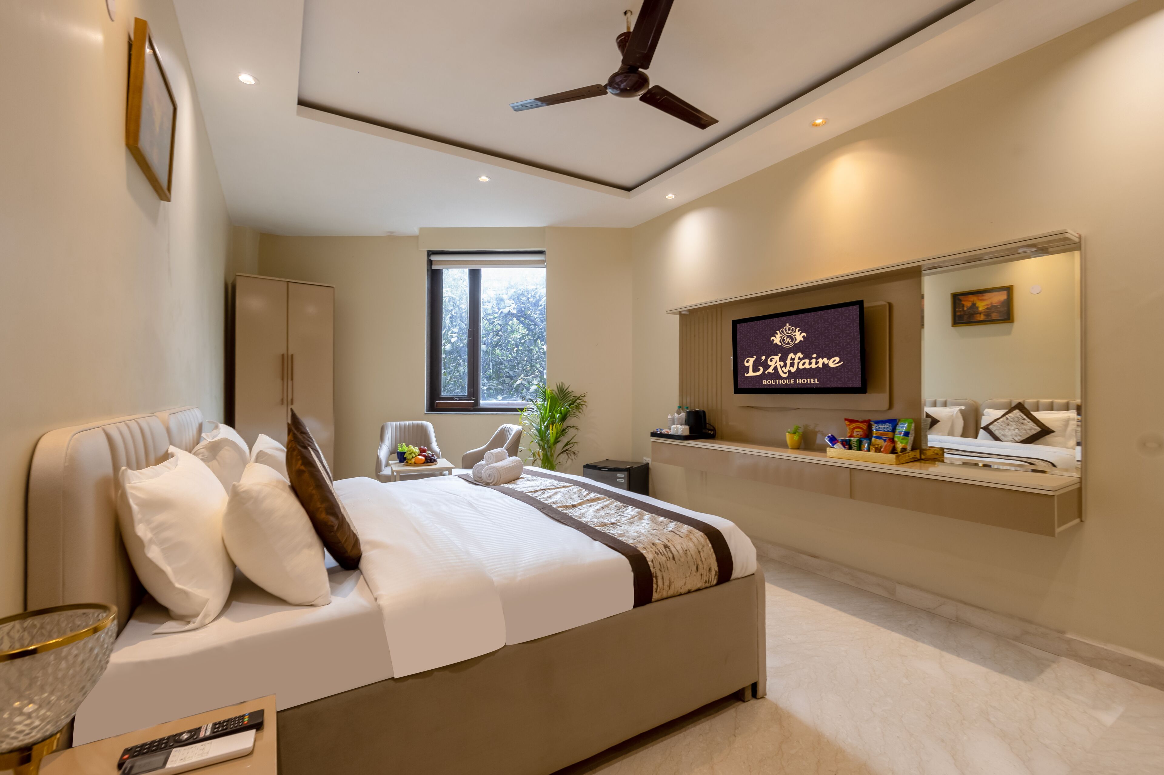 A modern hotel room with a large bed, a ceiling fan, a TV, and a window with a view of trees.