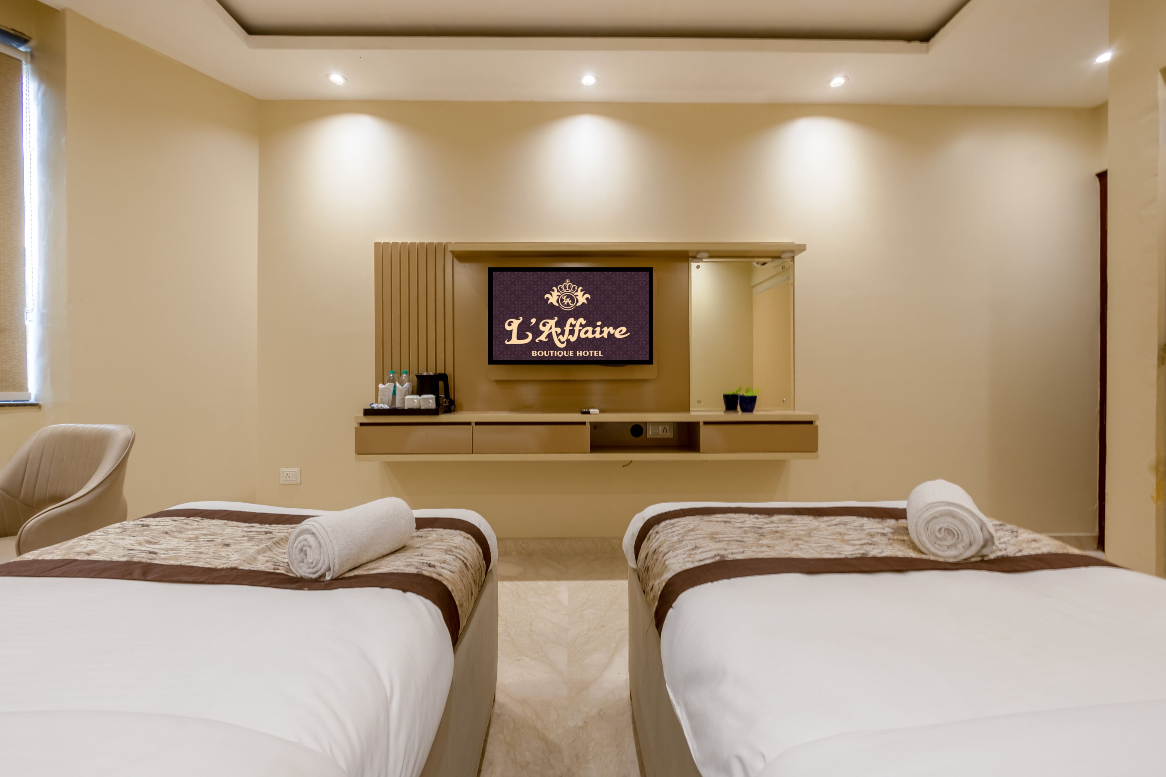 A hotel room with two beds, a TV, a mirror, a desk with a coffee machine, and a chair.