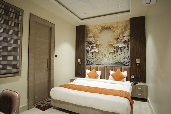 A hotel room with a bed, a nightstand, a desk, a chair, and a decorative wall piece. - Hotel Green Palace (Prayagraj)