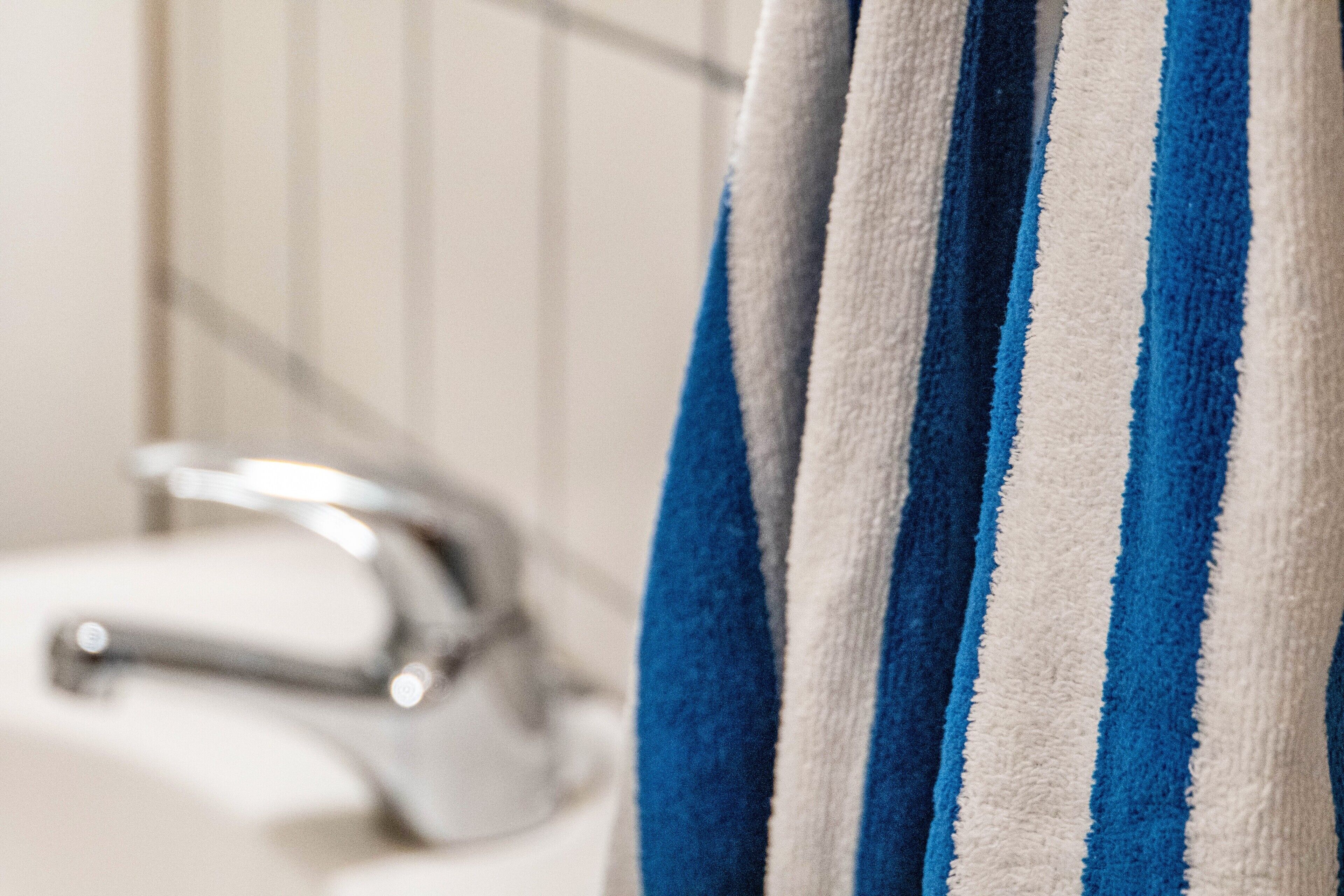 Une salle de bain avec une serviette à rayures suspendue à un porte-serviettes, un robinet chromé et des murs carrelés.
