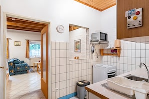 Una cocina compacta con microondas, estufa y lavamanos, un pequeño comedor con mesa y sillas, y un sofá en la sala de estar contigua.