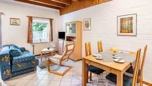 Een gezellige kamer met een bank, een eettafel met stoelen, een kast en een raam met gordijnen.