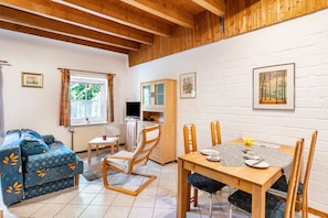 Una stanza accogliente con divano, tavolo da pranzo con sedie, credenza e finestra con tende.