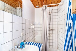 A bathroom with white tiled walls, a blue and white checkered bathtub, a shower with a wooden ceiling, and a blue and white striped towel. - Vacation at the uhlenhoff apartment hieve (Ihlow)