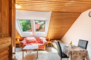 A cozy attic room with a sloped ceiling, a red patterned sofa, a small table, and a dining table with a floral tablecloth. - Vacation at the uhlenhoff apartment hieve (Ihlow)