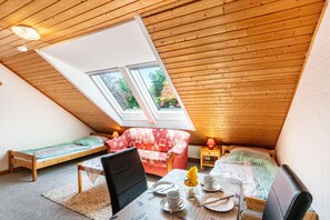 A cozy attic bedroom with a sloped ceiling, two windows, a bed, a sofa, a dining table with breakfast items, and a chair. - Vacation at the uhlenhoff apartment hieve (Ihlow)