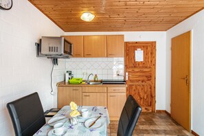 Une cuisine compacte avec des meubles en bois, un four à micro-ondes et un évier. On y trouve une table à manger avec des chaises et une horloge au mur.