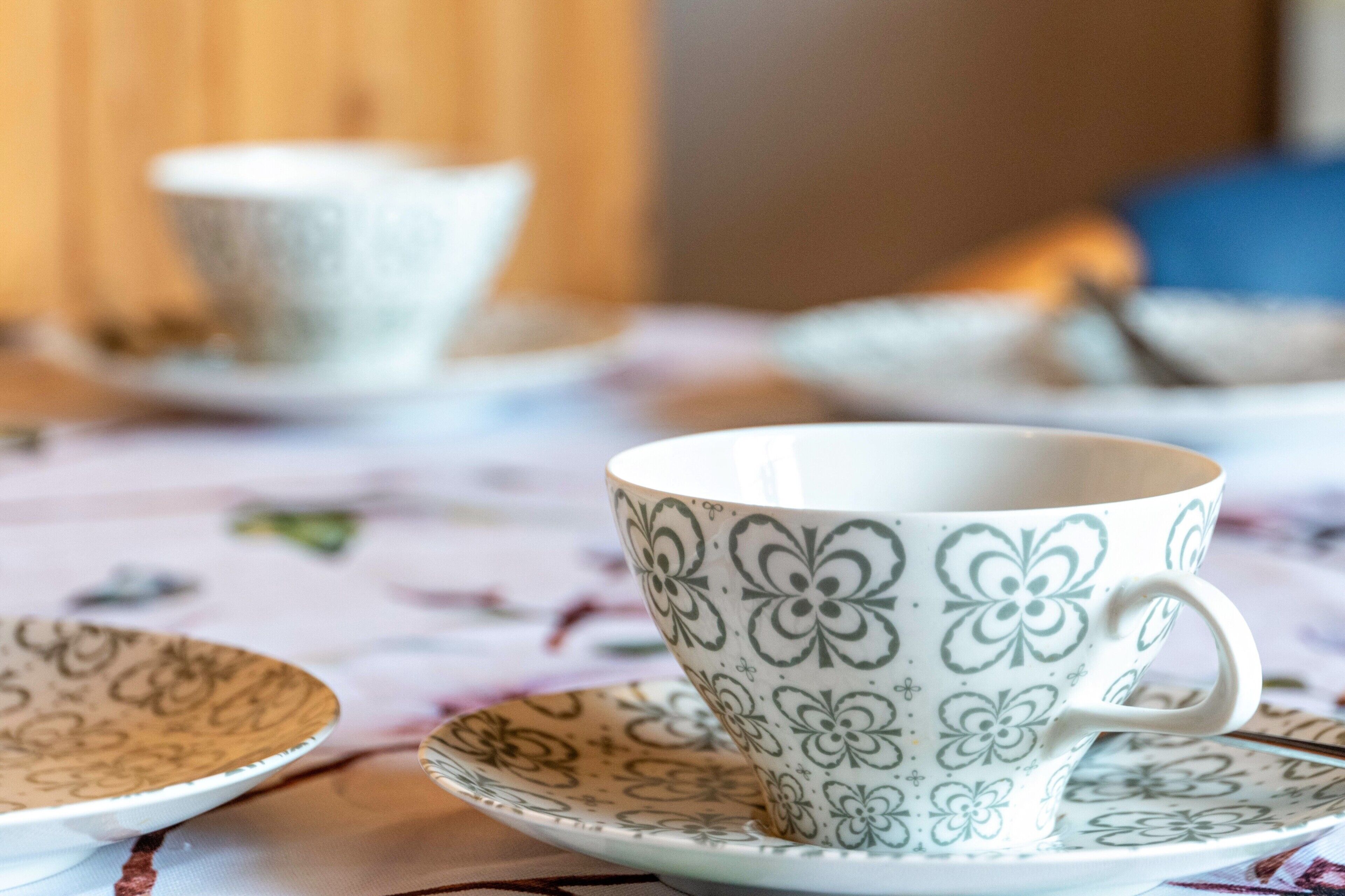 Une table recouverte d’une nappe à motifs floraux, une tasse et une soucoupe ornées de motifs floraux, et une assiette au même motif.