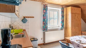 Een keuken met een raam, houten kastjes, een radiator en een tafel met een bloemen tafelkleed.