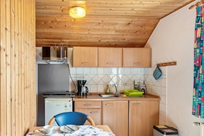 Una cocina compacta con armarios de madera, un refrigerador, una cafetera y un lavamanos.