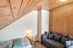 A room with a sloped ceiling, a bed with patterned bedding, a small bedside table with a lamp, and a sofa with cushions. - Vacation at the uhlenhoff apartment ewiges meer (Ihlow)